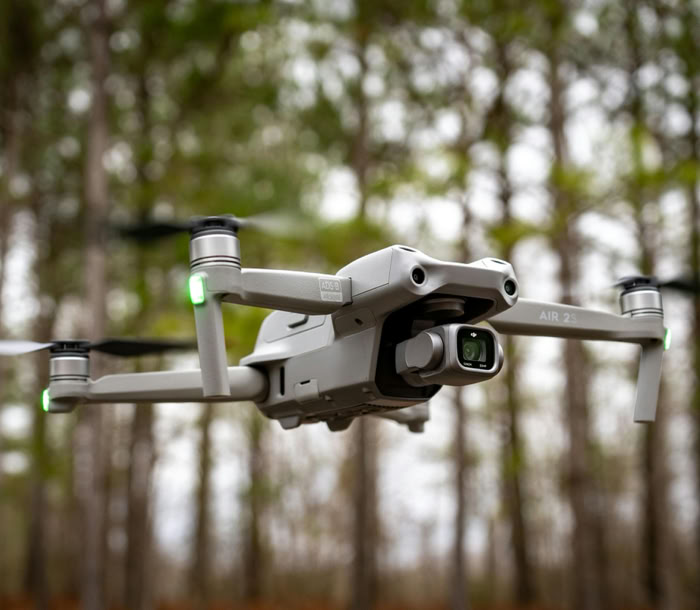 Close-up of a drone in midair with trees in the background, showcasing technology and nature.